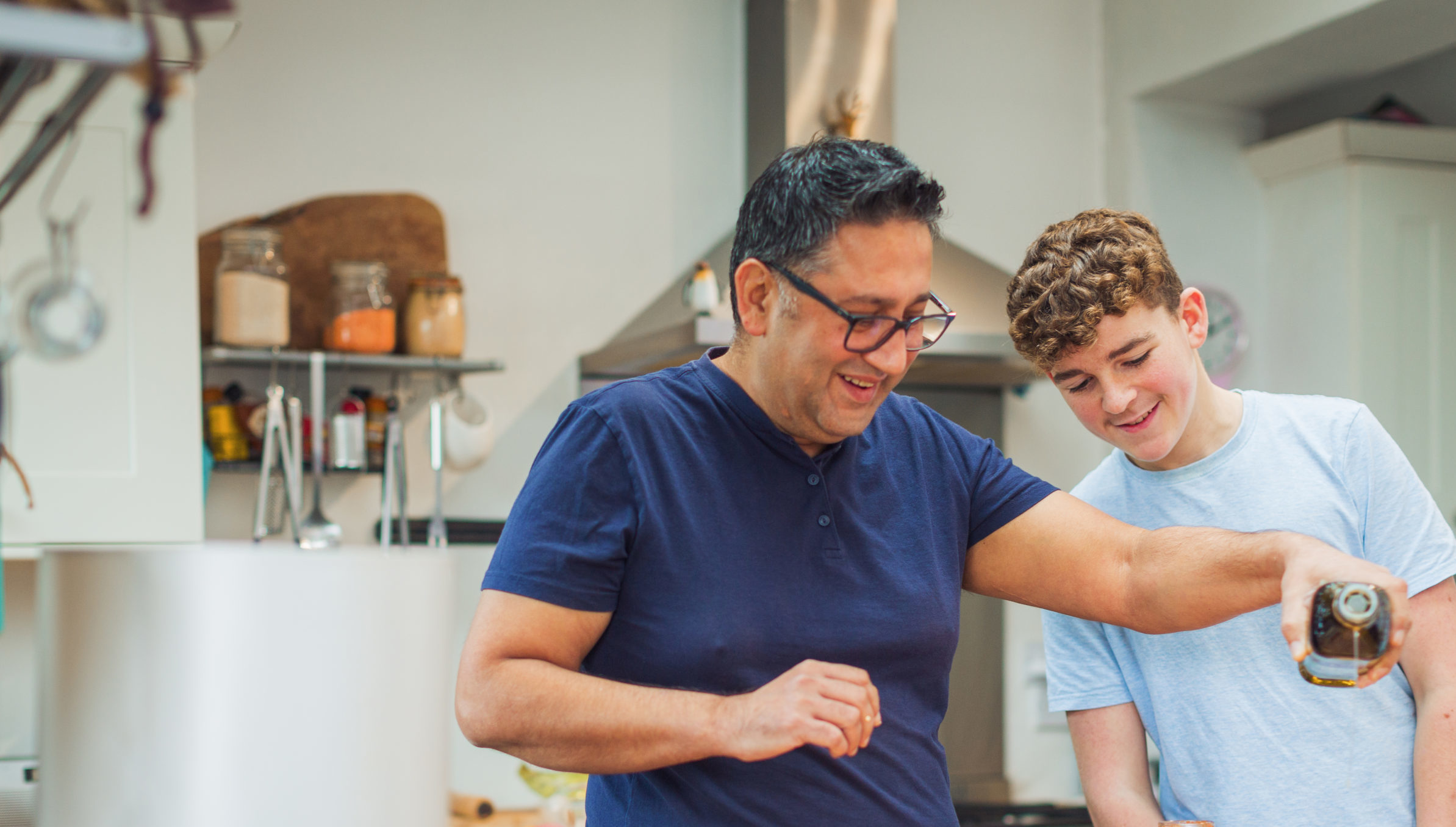 In the kitchen, an adult and a young boy make pizza together