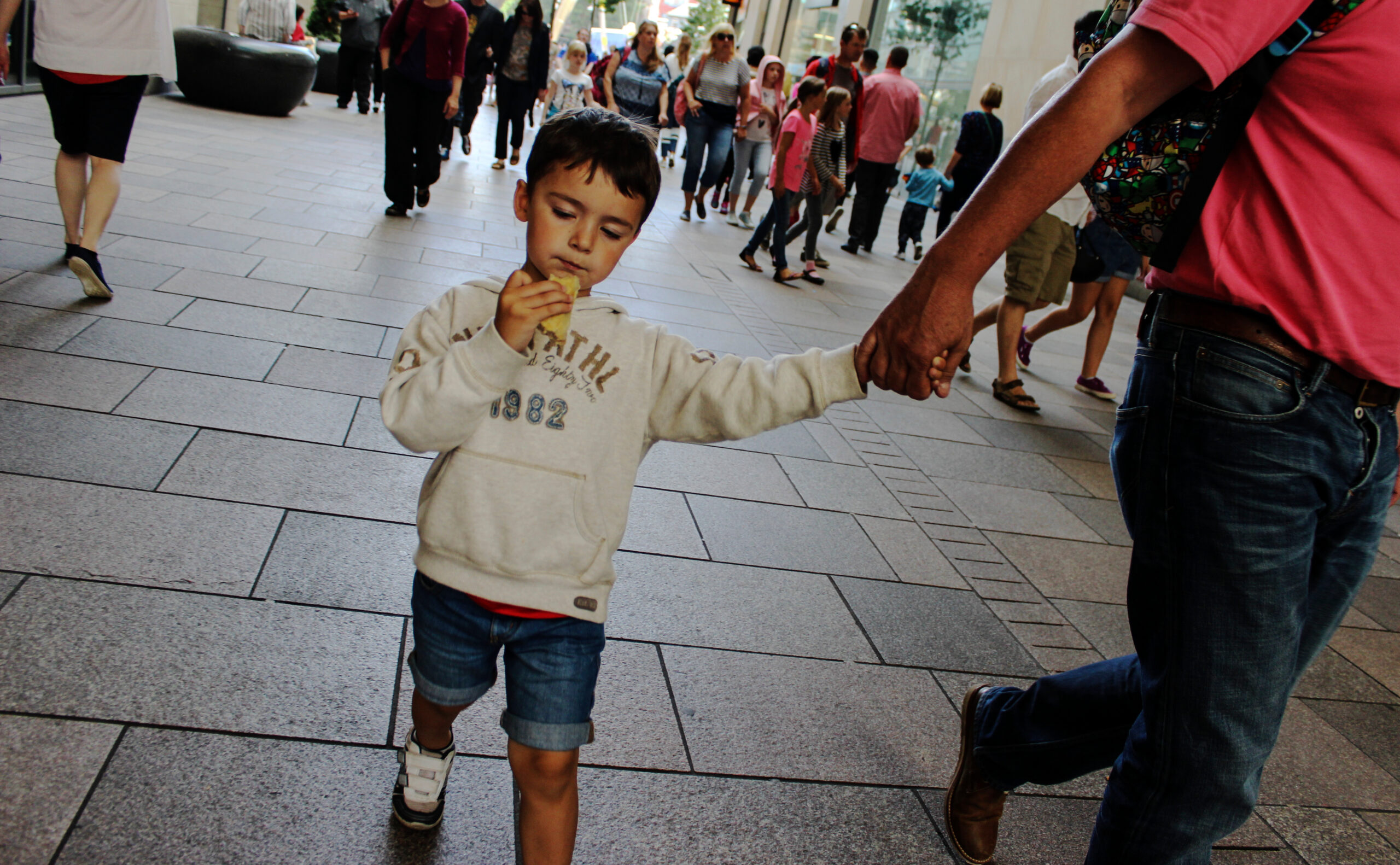 Boy child walking with father holding hands eating pastry